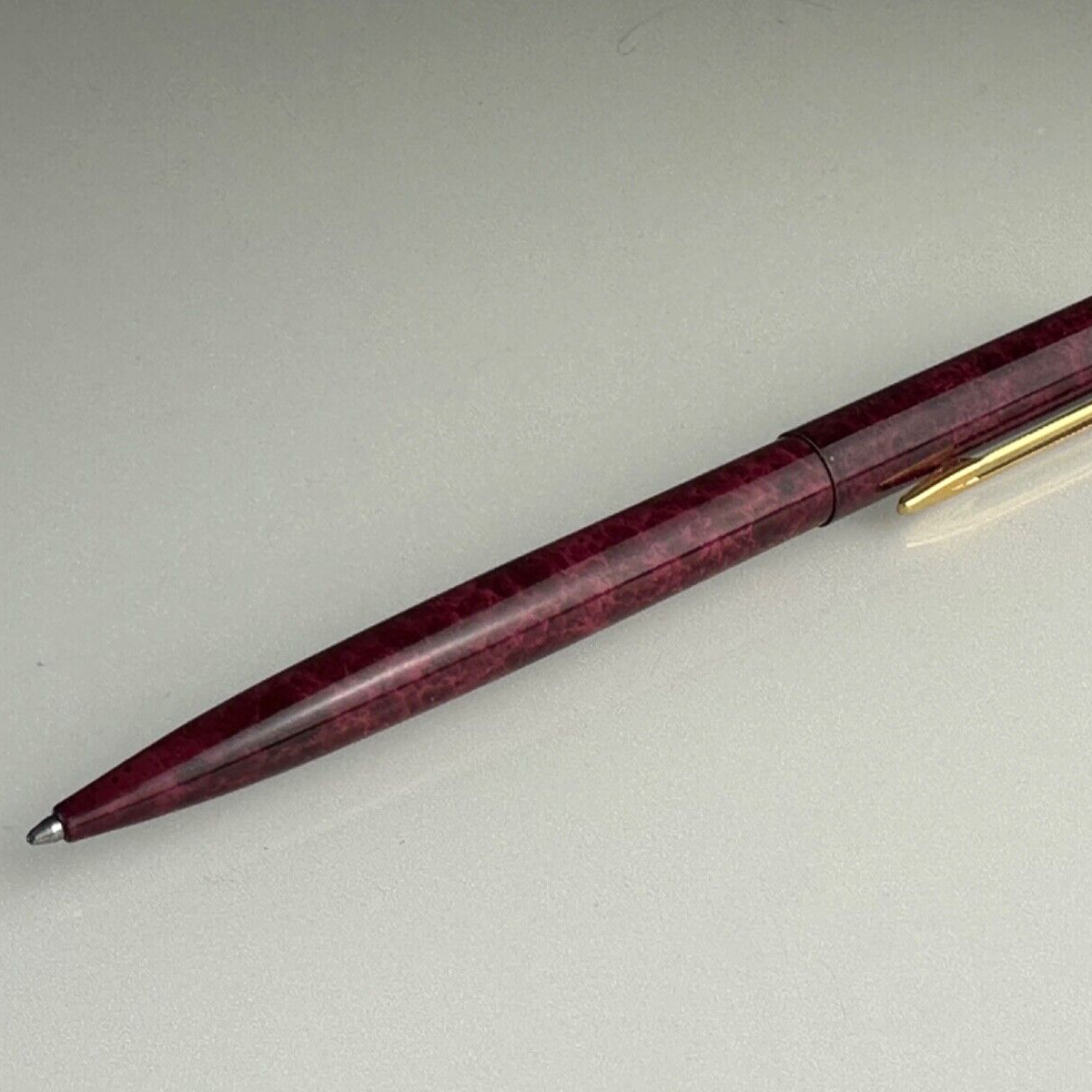 A Waterman ballpoint pen with a red gold body and bordeaux red ink, lying on a white surface.