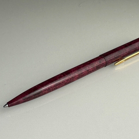A Waterman ballpoint pen with a red gold body and bordeaux red ink, lying on a white surface.
