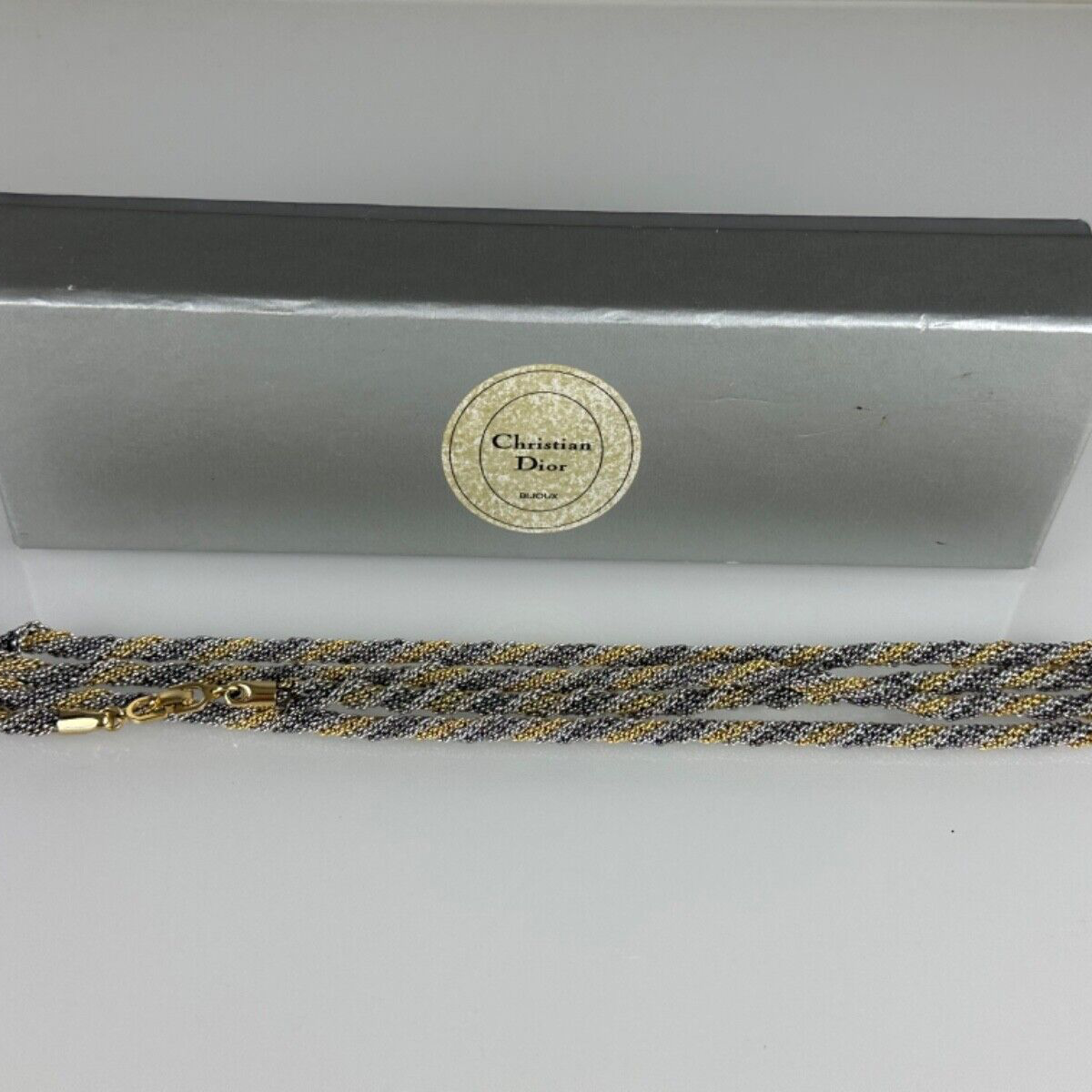 A vintage Christian Dior necklace with gold and silver colors, displayed alongside its original box.