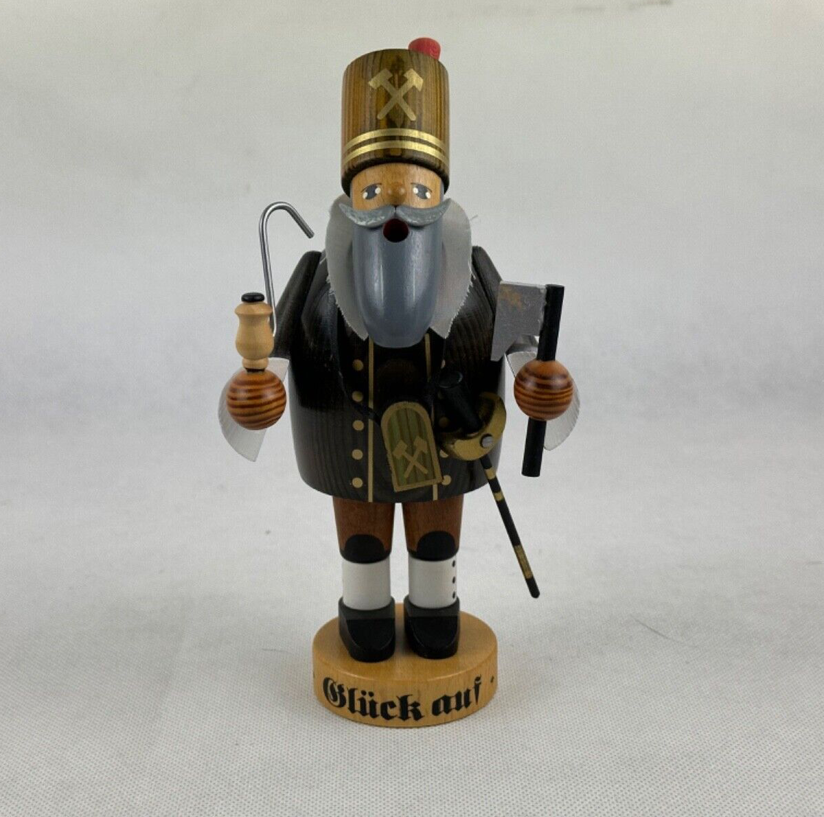 A wooden incense smoker figurine dressed as a miner with a 'Glück Auf' sign, holding a pipe and a bottle, standing on a round base.